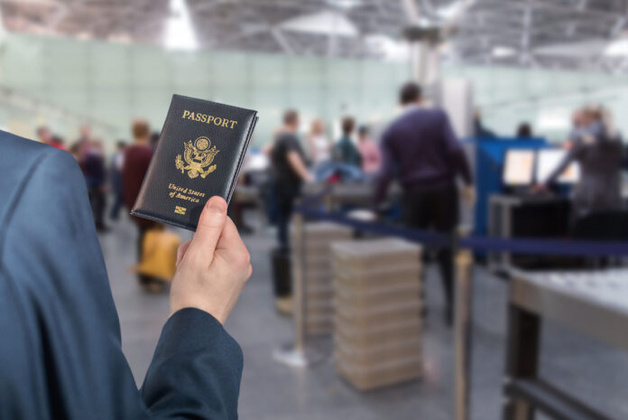 Man (businessman) in a blue suit with suitcase holding american passport with boarding pass in the airport opposite customs control or security service . concept.